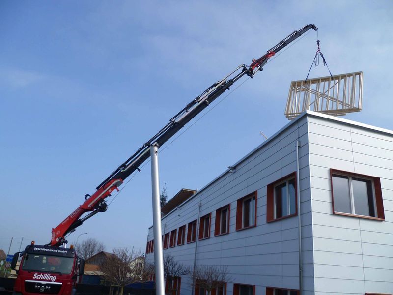 Ein Kran hebt ein Stück Holz auf ein Gebäude. Foto von der Mannhart Holzbau AG
