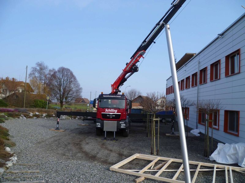 Ein roter LKW mit einem daran befestigten Kran steht vor einem Gebäude