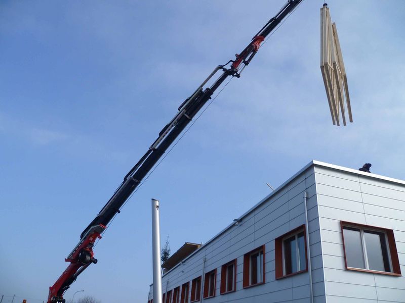 Ein großer Kran hebt ein Stück Holz über ein Gebäude