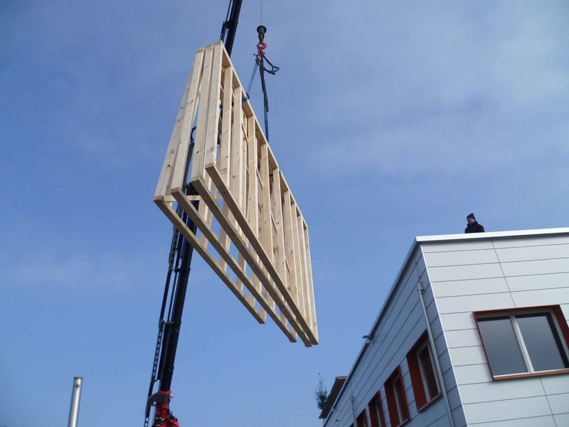 Ein grosses Stück Holz wird von einem Kran angehoben. Foto von der Mannhart Holzbau AG