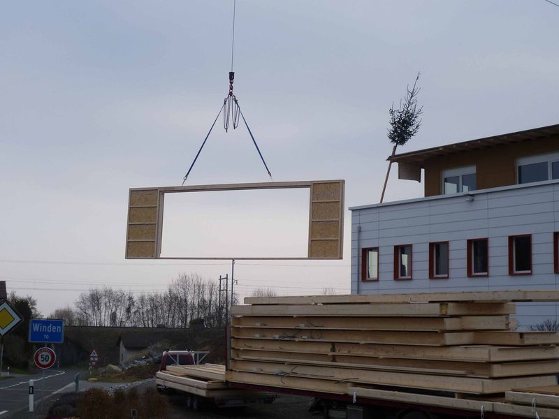 Ein grosses Stück Holz wird von einem Kran angehoben. Foto von der Mannhart Holzbau AG