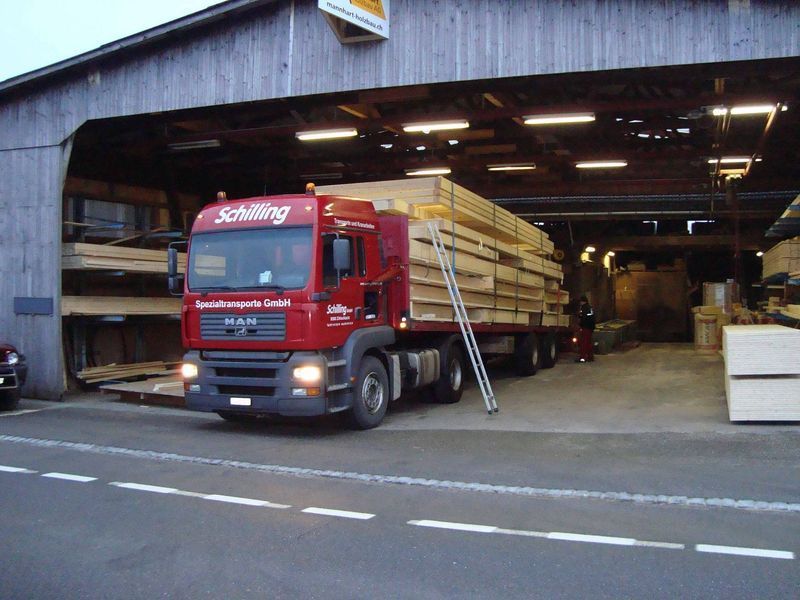 Ein roter Lastwagen transportiert Holz. Foto von der Mannhart Holzbau AG