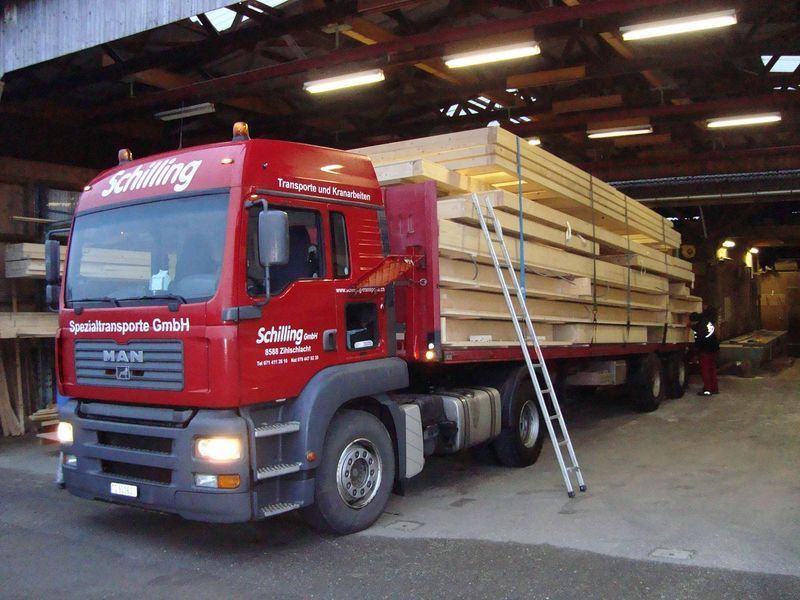 Ein roter Lastwagen transportiert Holz. Foto von der Mannhart Holzbau AG