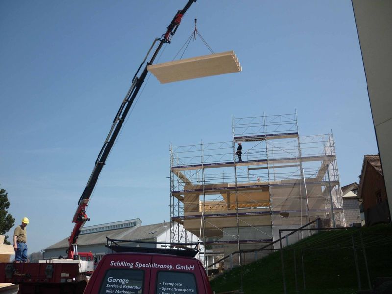 Ein Kran hebt ein Stück Holz über ein Gebäude. Foto von der Mannhart Holzbau AG