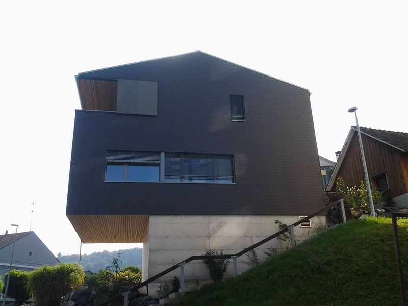 Ein rotes Haus steht auf einem grasbewachsenen Hügel. Foto von der Mannhart Holzbau AG 