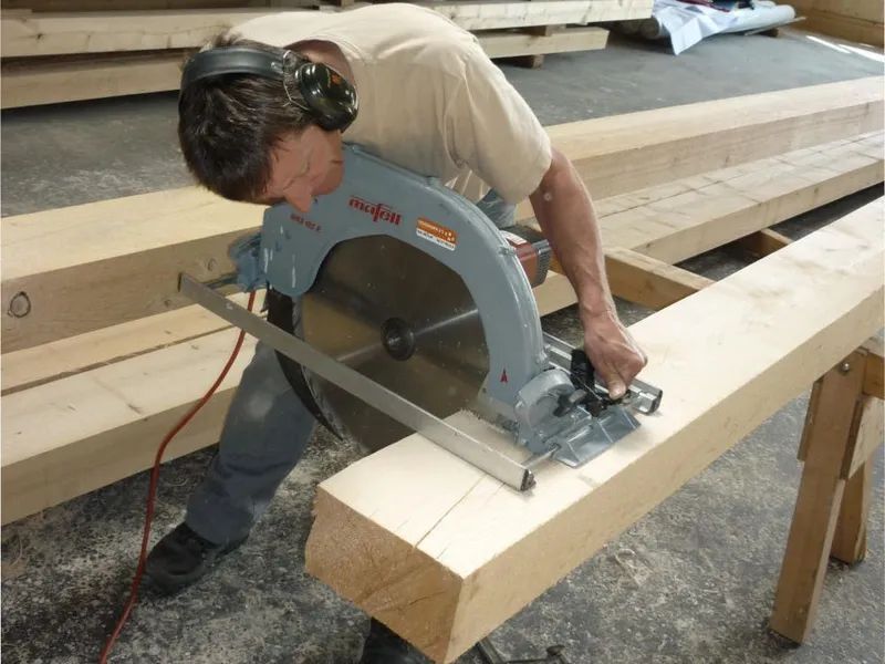 Ein Mann schneidet mit einer Kreissäge ein Stück Holz. Foto von der Mannhart Holzbau AG