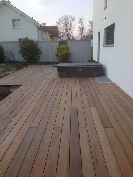 Eine Holzterrasse mit einem Whirlpool im Hinterhof eines Hauses.