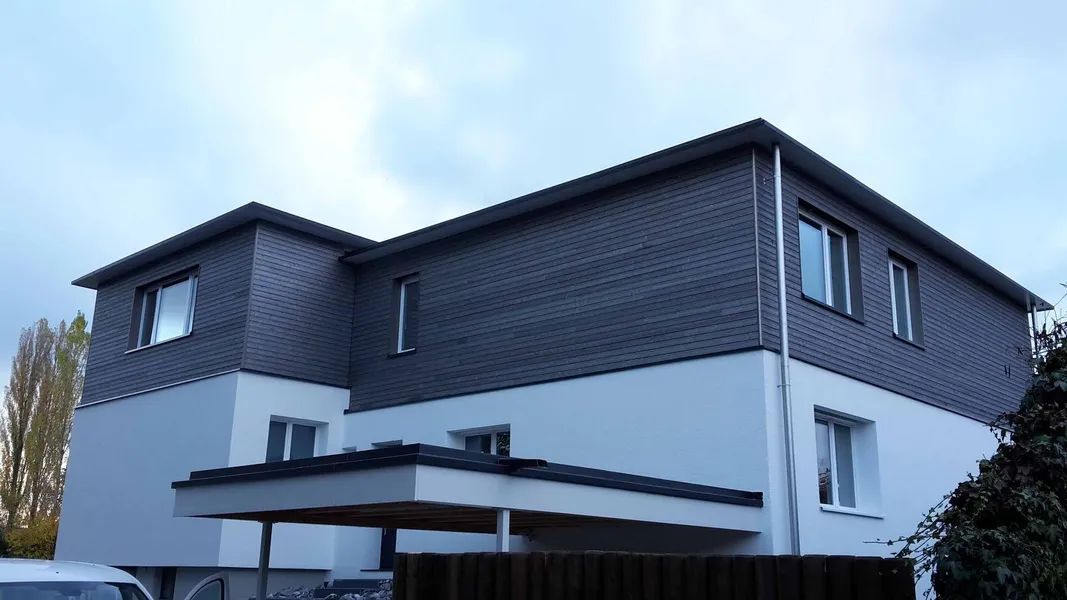 Ein großes weiß-schwarzes Haus mit einem Carport davor.