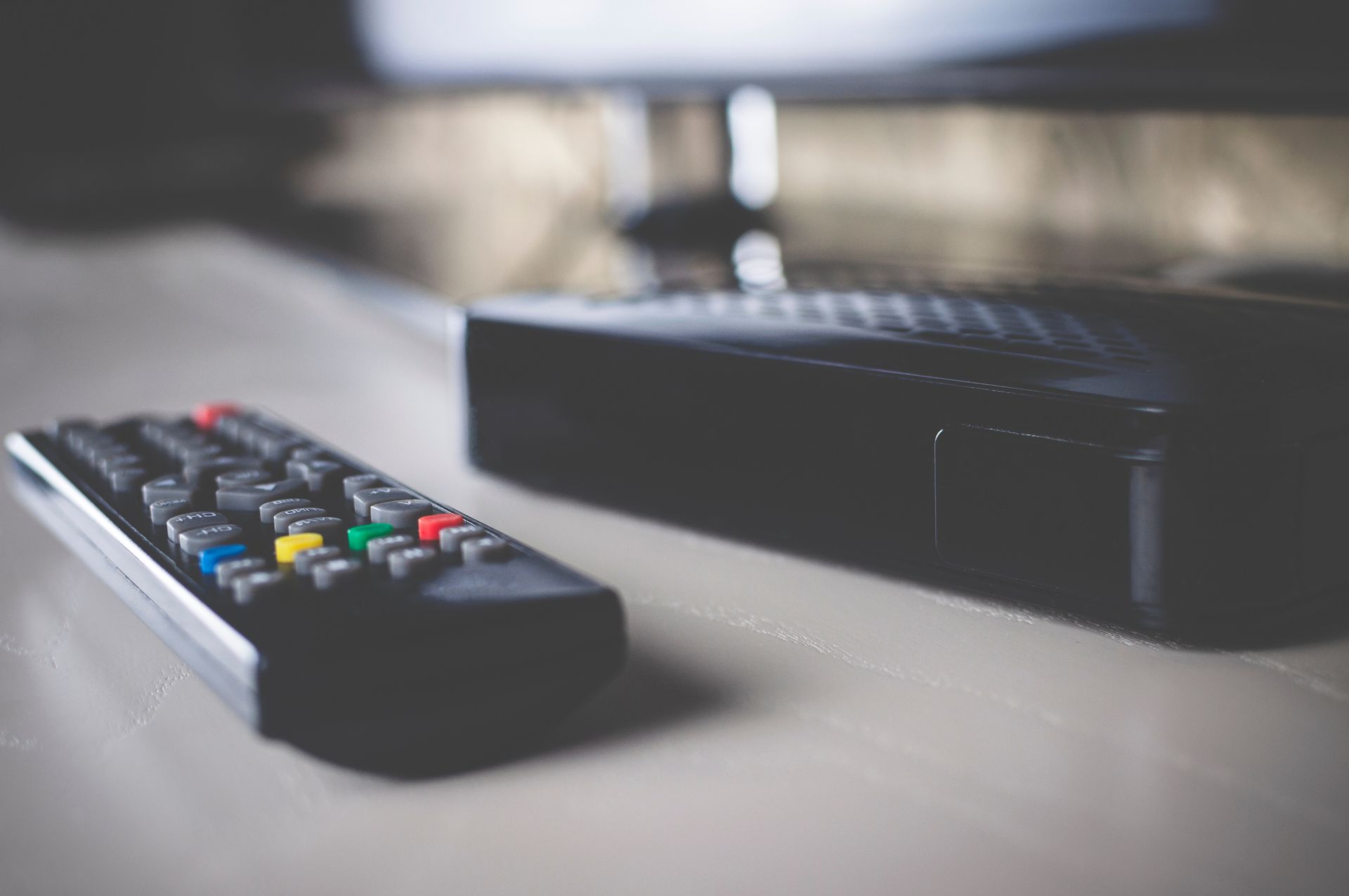 Gros plan sur une télécommande, un boîtier TNT et le bas d'une télévision