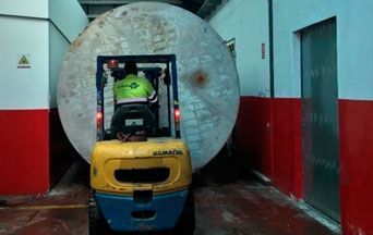 Un hombre conduce una carretilla elevadora en un garaje transportando un objeto grande.