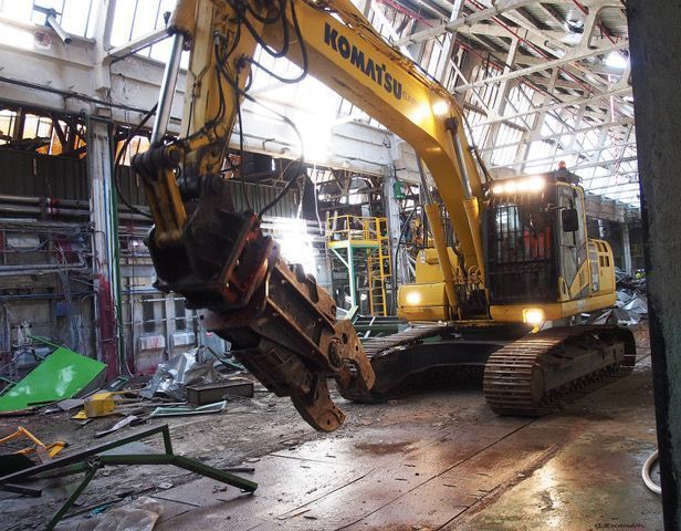 Se está utilizando una excavadora Komatsu para demoler un edificio en una fábrica.