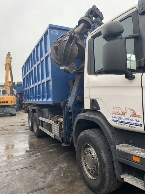 Un camión blanco está estacionado al lado de un contenedor de basura azul.