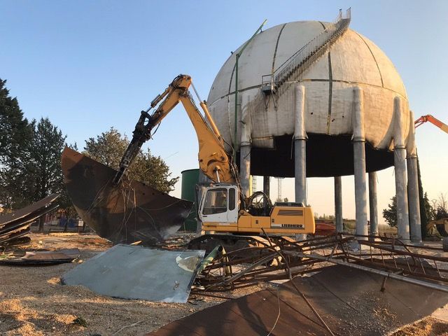 Una excavadora amarilla está demoliendo una torre de agua.