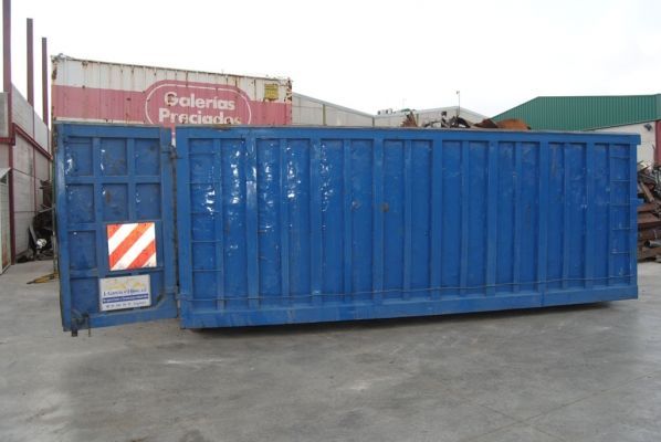 Un gran contenedor de basura azul está estacionado frente a un edificio que dice