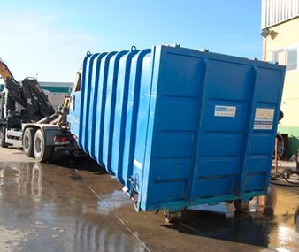 Un gran contenedor de basura azul está siendo remolcado por un camión.