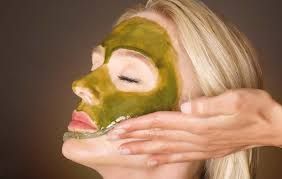 Eine Frau bekommt eine Gesichtsbehandlung mit einer grünen Maske im Gesicht.