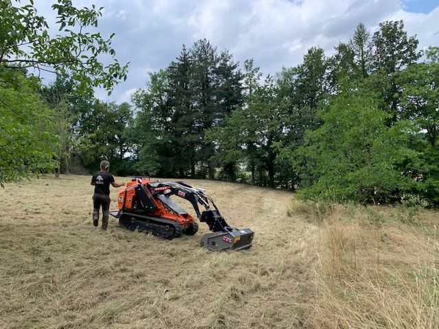 Véhicule tout-terrain orange dans un champ avec de l'herbe, une personne se tenant à côté sous un ciel nuageux.