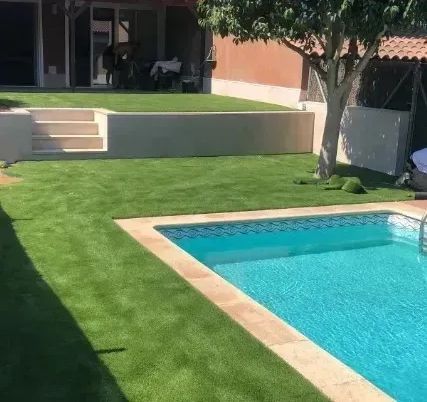 Patio trasero con piscina, césped verde, escalones de patio y un árbol que da sombra junto a una casa.