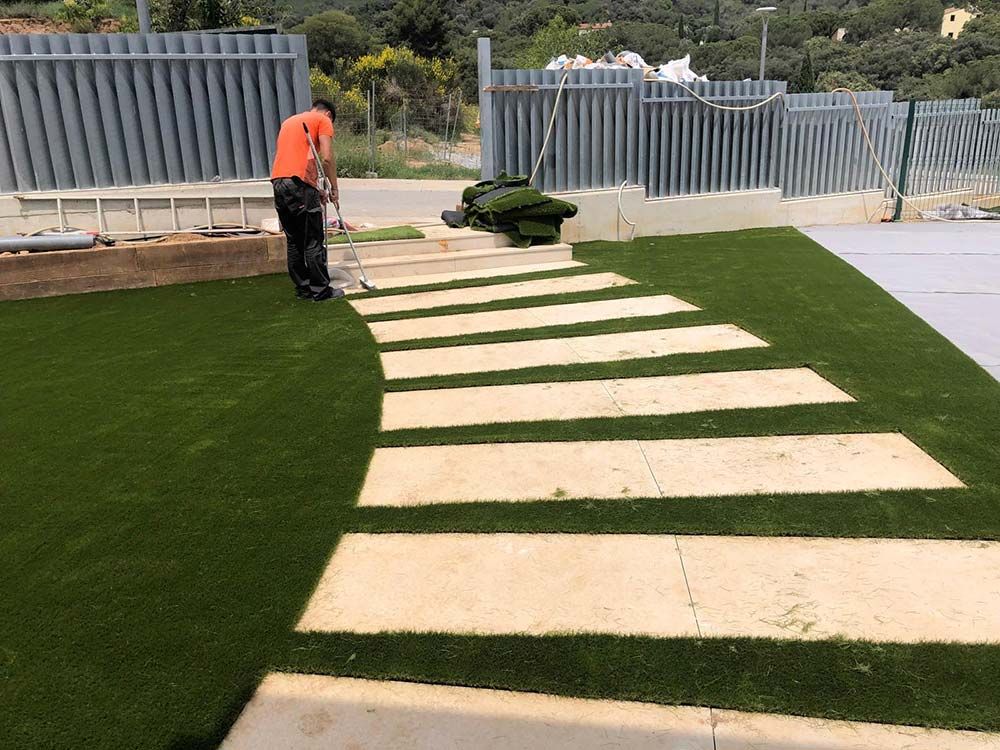Un trabajador coloca losas de color beige en un sendero de césped artificial verde al aire libre.