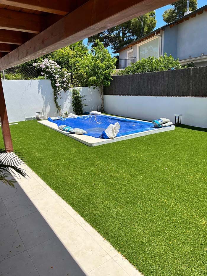 Patio trasero con césped verde, piscina cubierta y terraza de madera en un día soleado.