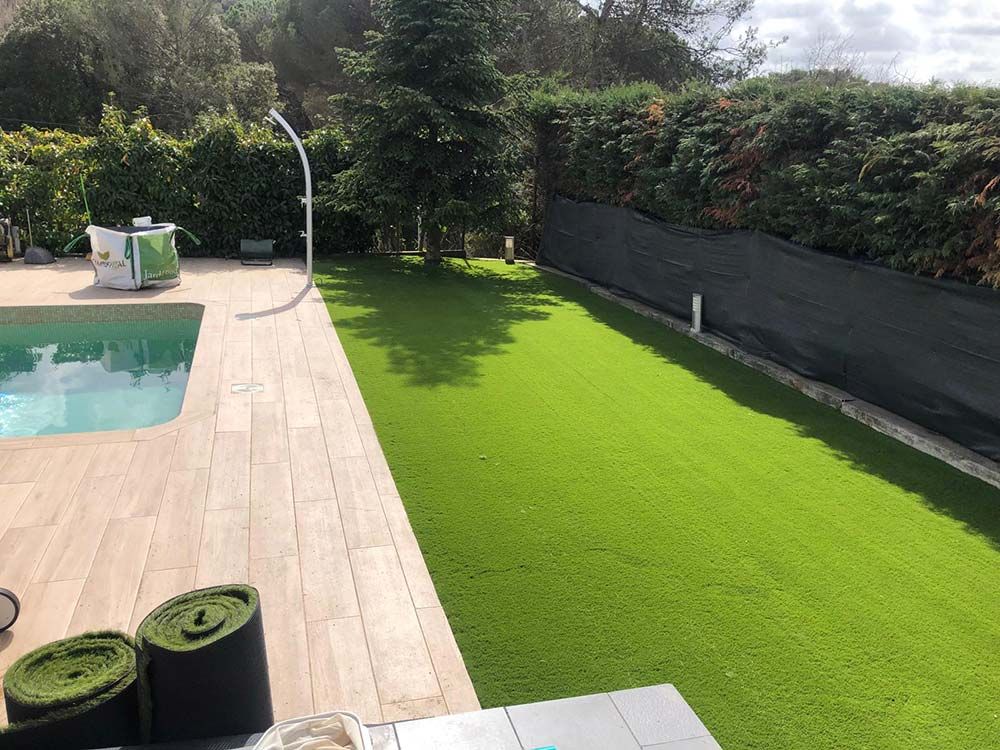 Terraza trasera con césped verde brillante y tumbonas junto a una piscina de color turquesa.