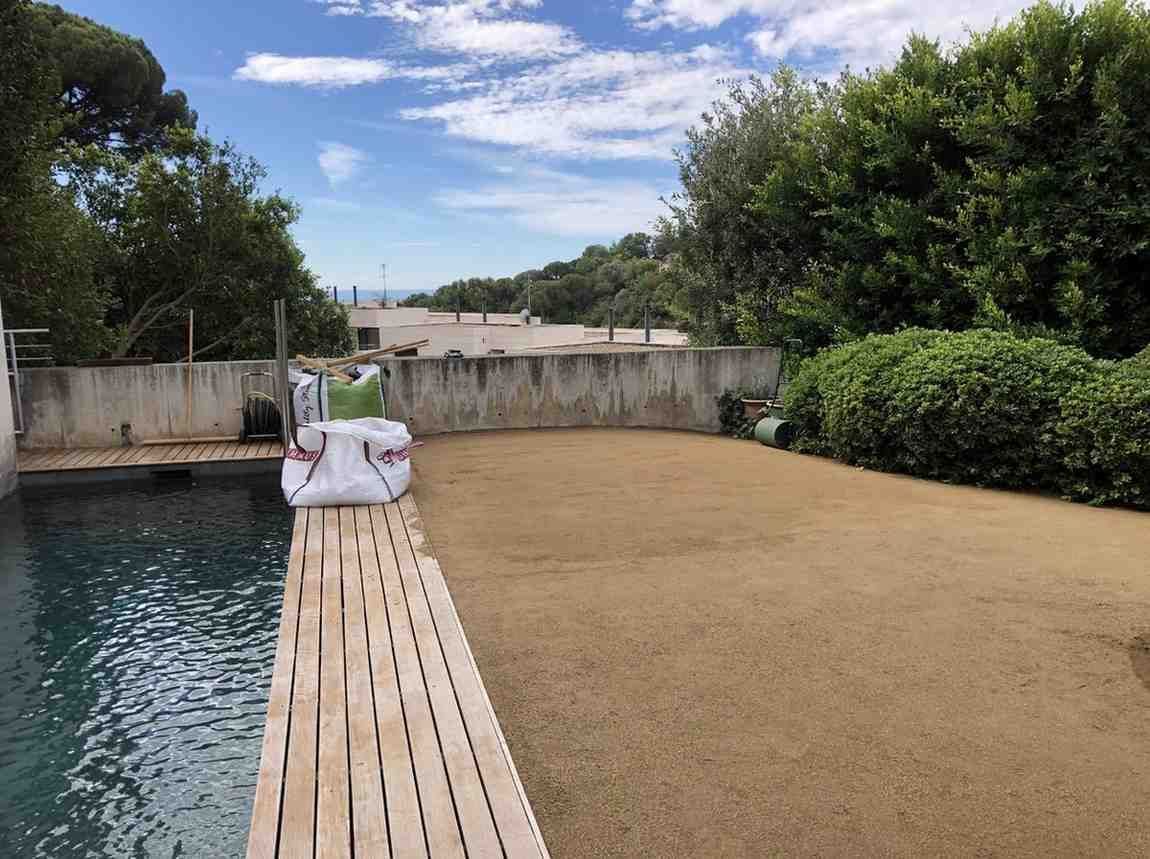 Piscina en el patio trasero con trampolín, terraza para tomar el sol y árboles bajo un cielo nublado.