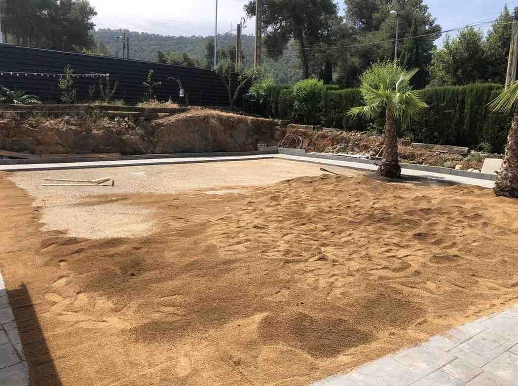 Patio trasero seco y arenoso con una pequeña piscina vacía y árboles al fondo.