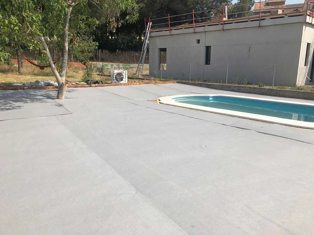 Terraza vacía junto a una pequeña piscina y un edificio gris bajo los árboles al aire libre.