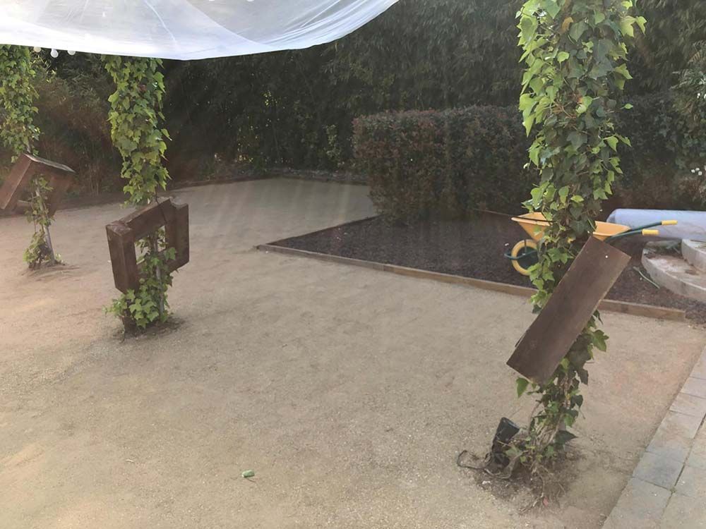 Patio lluvioso con hormigón mojado, toldo blanco colgante y macetas con plantas a lo largo de los bordes.