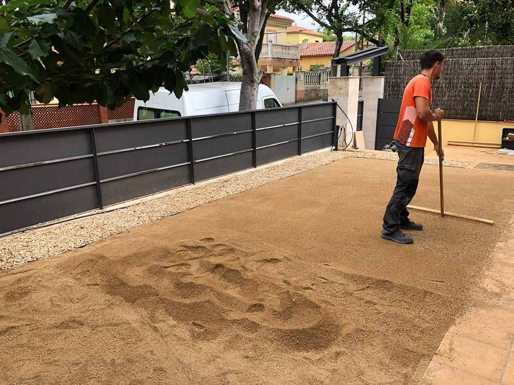 Un trabajador nivela la tierra en un patio con un rastrillo cerca de una cerca y una casa.