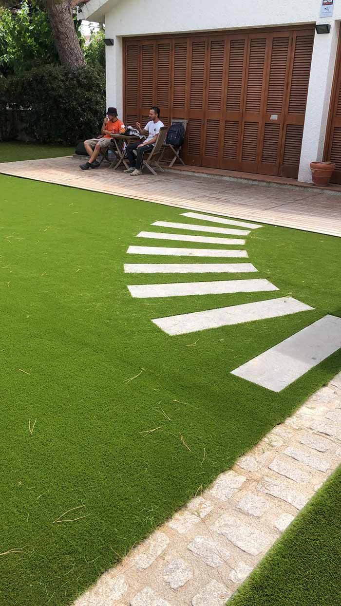 Losas blancas curvas sobre un césped verde brillante junto a una casa con una puerta de garaje de madera y gente sentada.