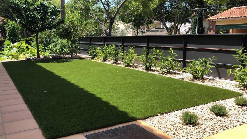 Pequeño jardín paisajístico con césped verde brillante, parterre y valla de madera bañado por el sol.