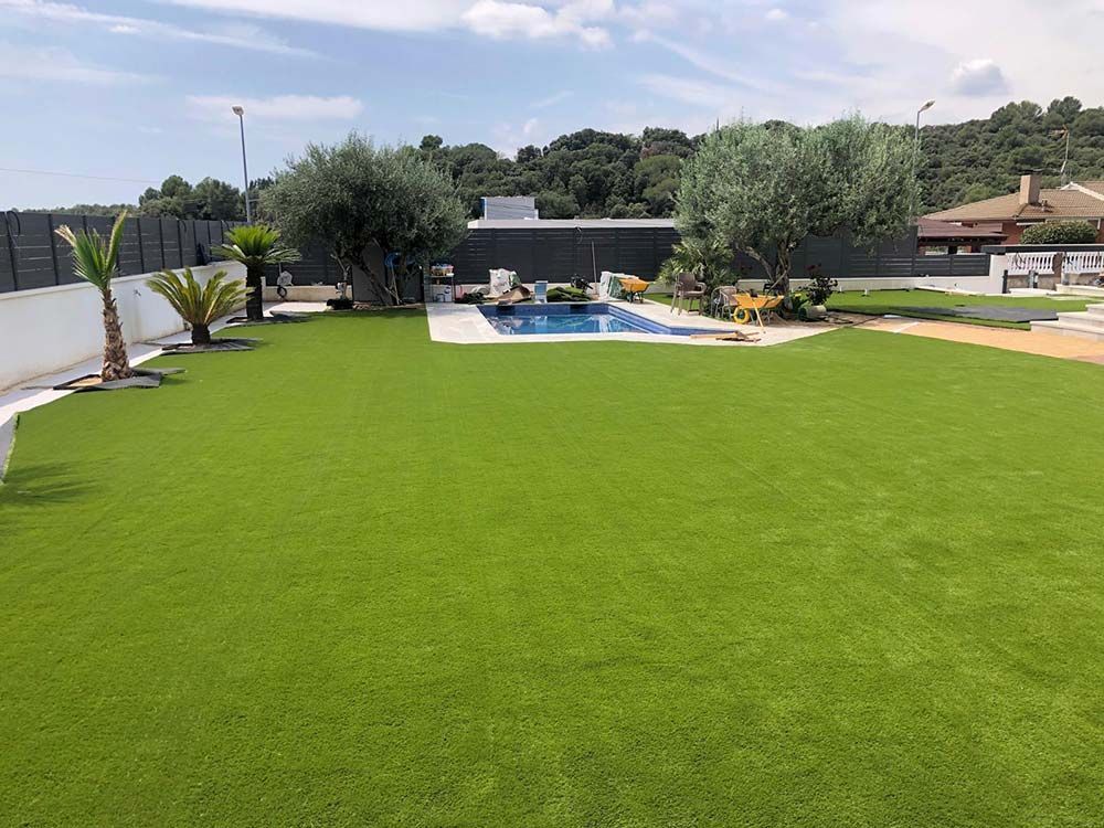 Amplio césped verde con piscina en el patio trasero, terraza y árboles bajo un cielo despejado.
