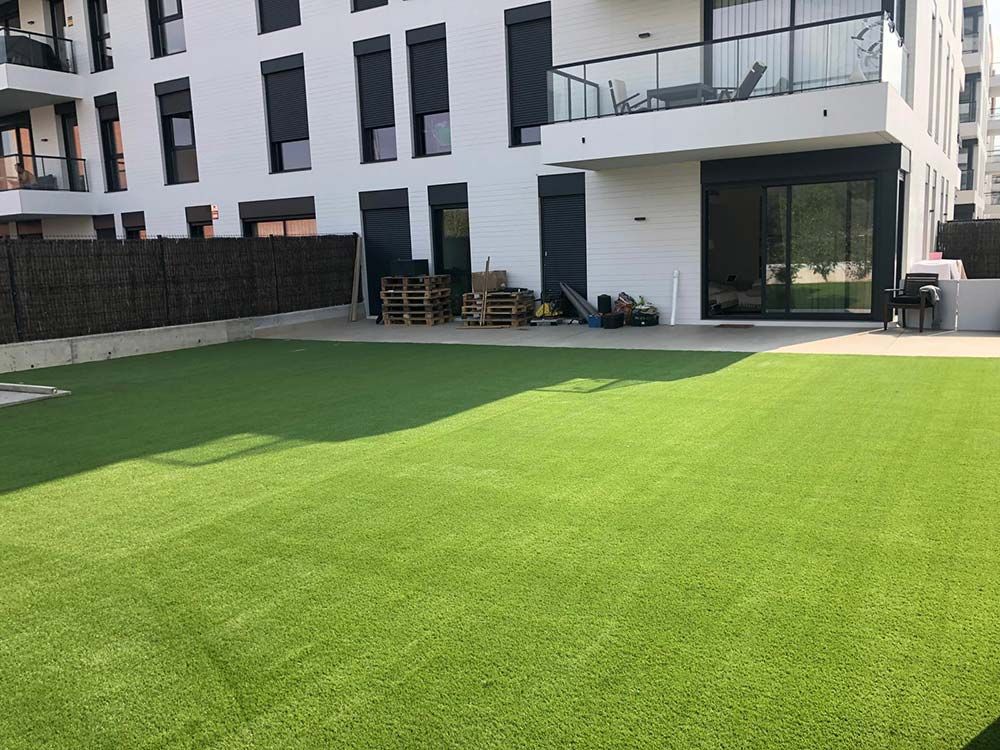 Edificio de apartamentos moderno con jardín y puertas correderas que dan a un balcón.