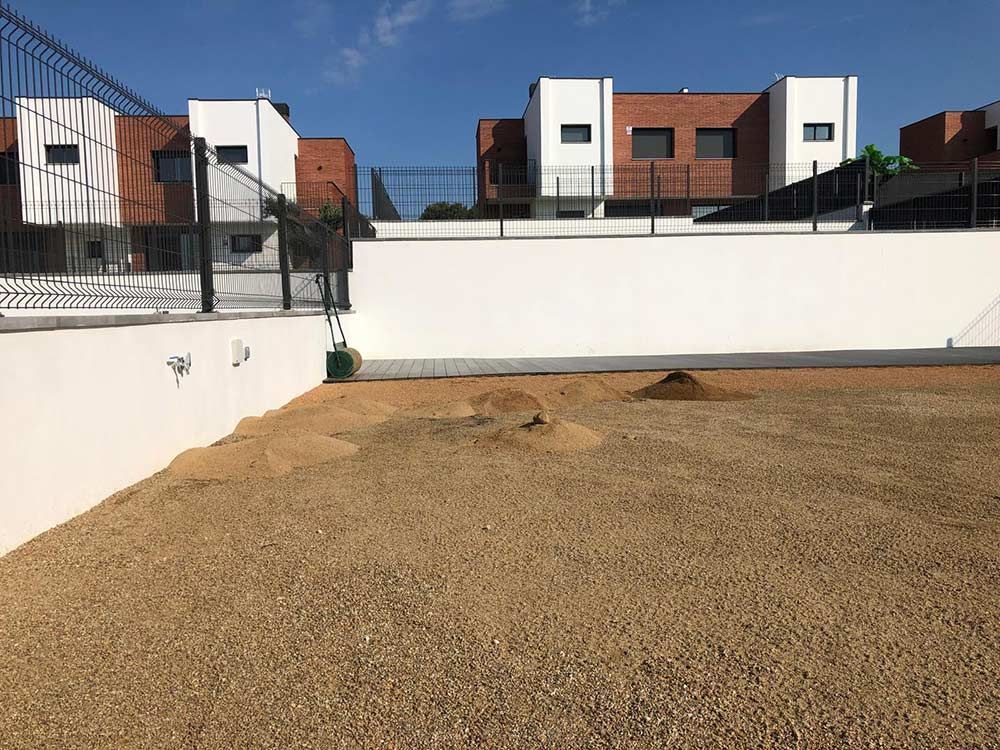 Patio trasero con suelo de grava, muros de contención blancos y casas de ladrillo al fondo.