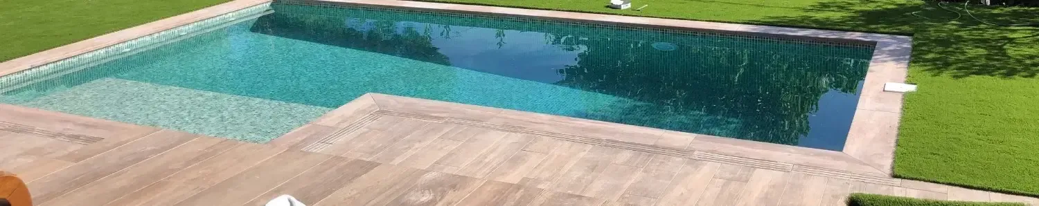 Piscina en el patio trasero con agua turquesa, terraza de piedra beige y césped verde.