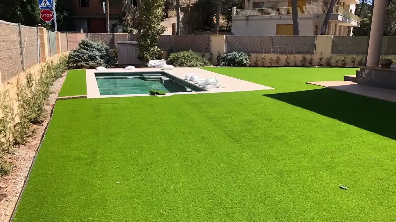Jardín trasero con césped verde brillante y piscina rectangular junto a un patio de piedra.