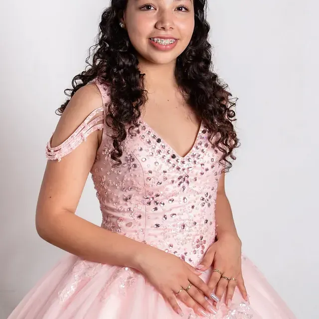 Una mujer con un vestido rosa está parada frente a una pared blanca.