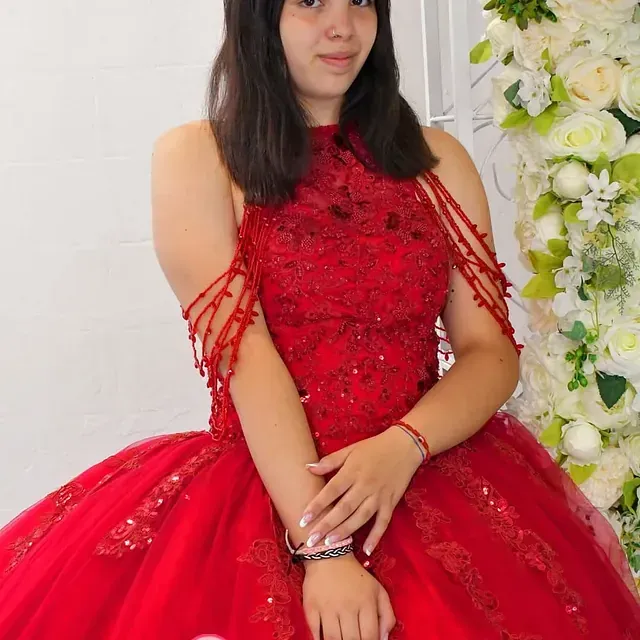 Una mujer con un vestido rojo está parada frente a una pared de flores.