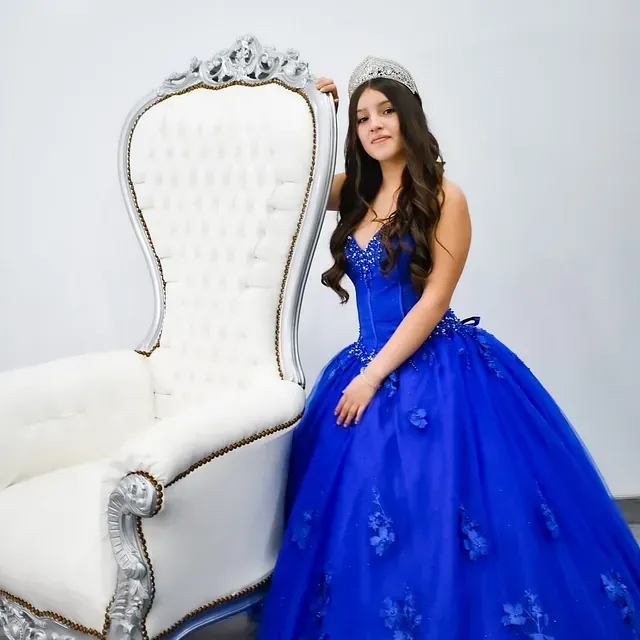 Una mujer con un vestido azul está de pie junto a una silla blanca.