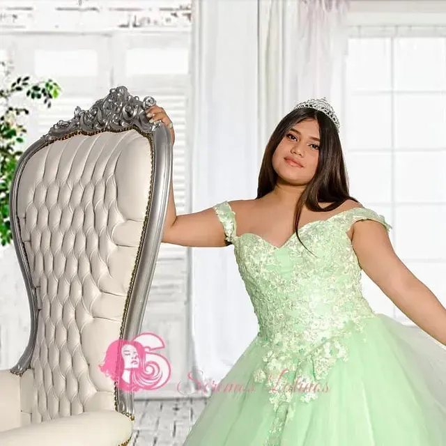 Una mujer con un vestido verde está de pie junto a una silla.