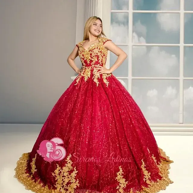Una mujer con un vestido de fiesta rojo y dorado está parada frente a una ventana.
