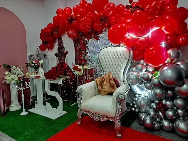 Una silla está sentada frente a una pared de globos rojos y plateados.