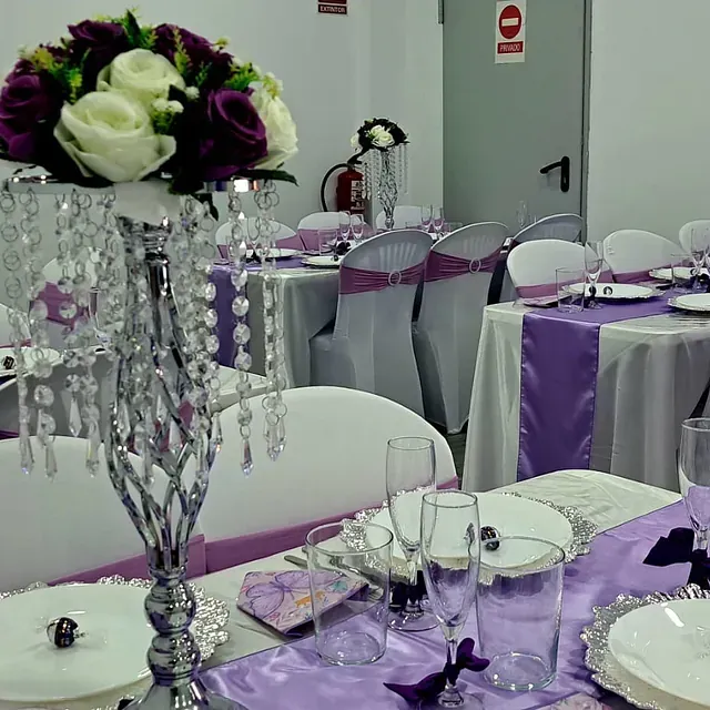 Una mesa preparada para una recepción de boda con decoraciones moradas y plateadas.