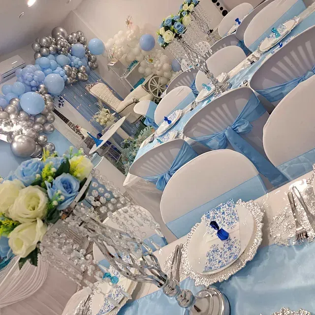 Una sala con mesas y sillas preparadas para una fiesta con decoraciones azules y plateadas.