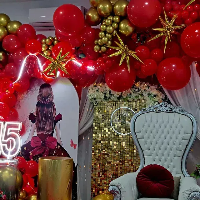 Una habitación decorada con globos rojos y dorados y una silla.