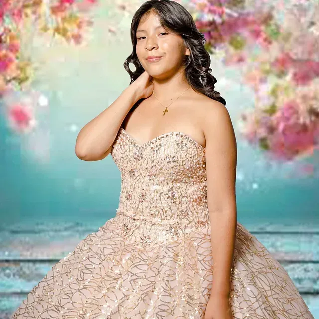 Una mujer con un vestido de gala está parada frente a un fondo floral.