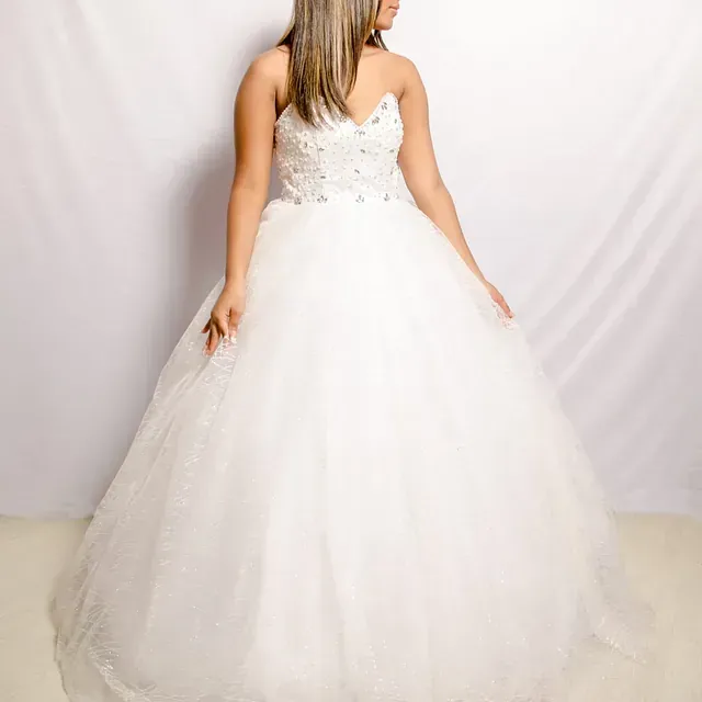 Una mujer con un vestido de novia blanco está parada frente a una cortina blanca.