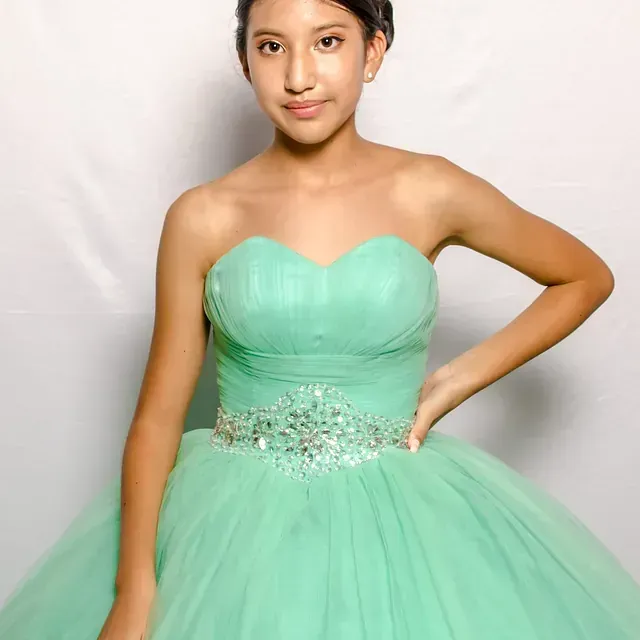 Una mujer con un vestido verde está parada frente a una pared blanca.