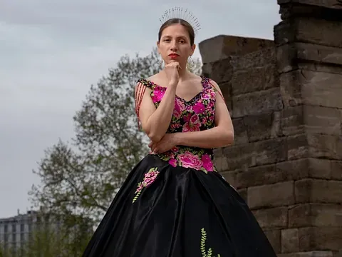 Una mujer con un vestido negro y rosa está parada frente a una pared de ladrillos.